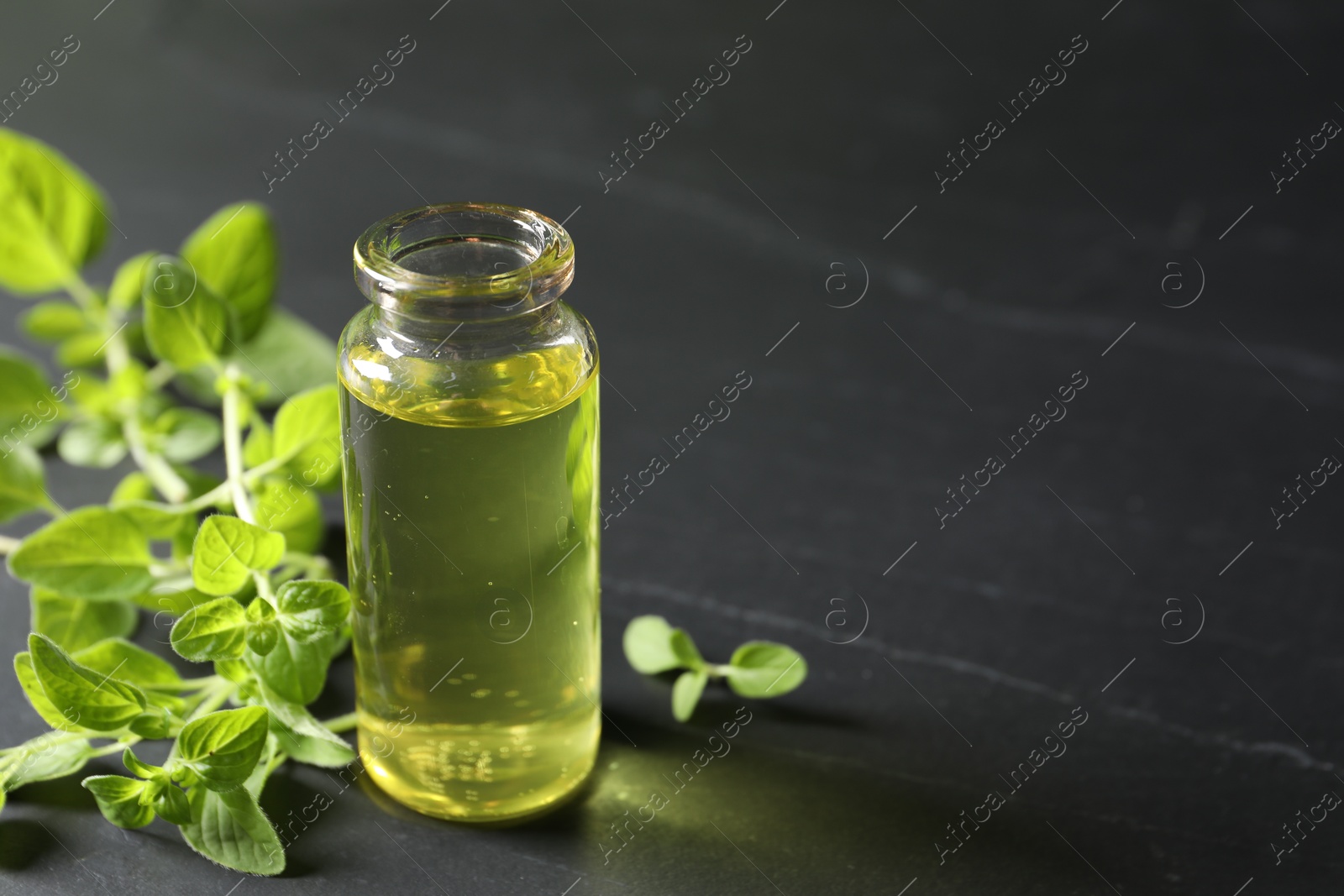 Photo of Essential oil in bottle and oregano twigs on dark textured table, closeup. Space for text