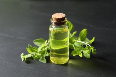 Photo of Essential oil in bottle and oregano twigs on dark textured table, closeup