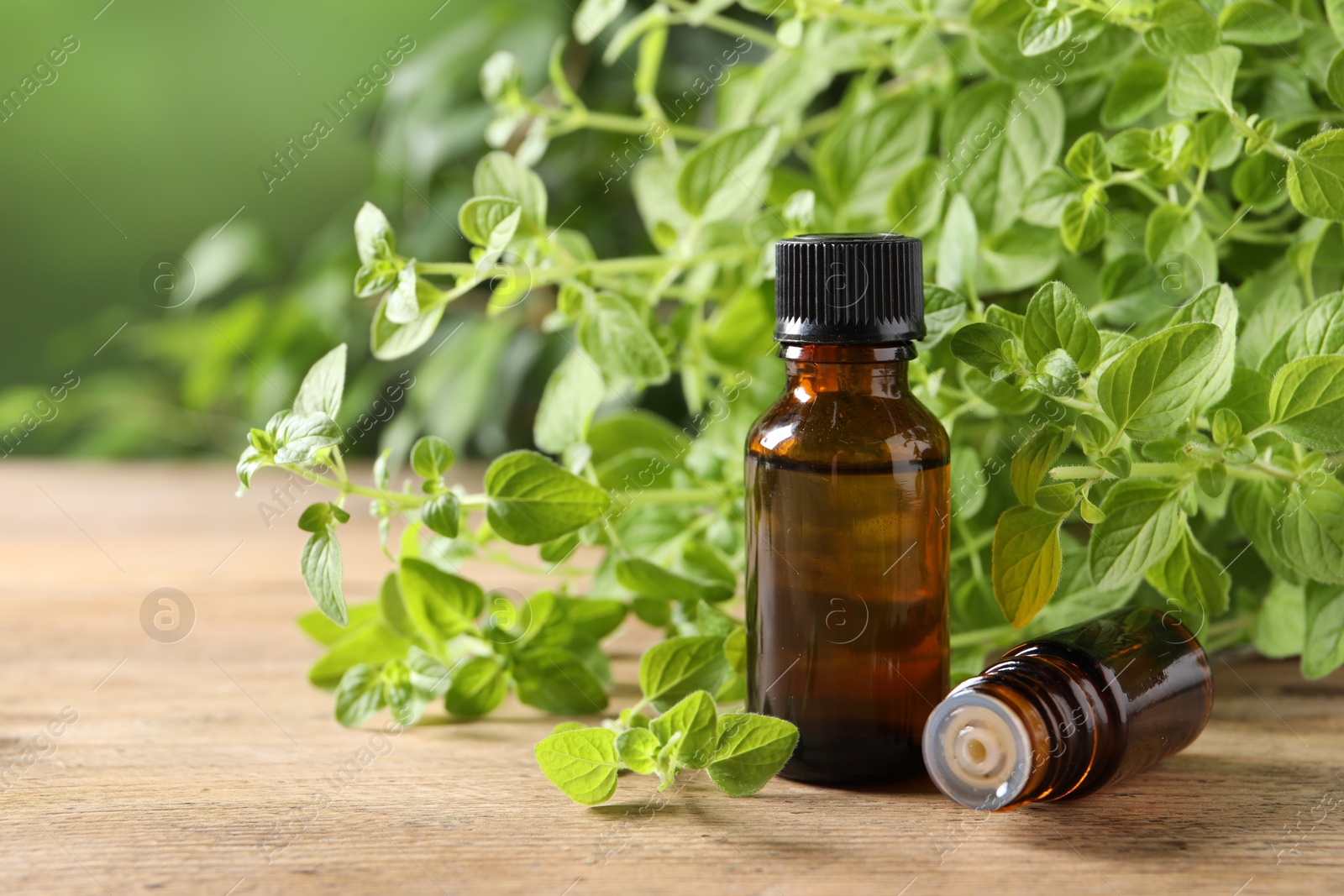 Photo of Essential oil in bottles and oregano twigs on wooden table against blurred green background, closeup. Space for text