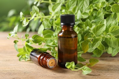 Photo of Essential oil in bottles and oregano twigs on wooden table, closeup