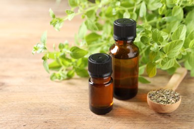 Photo of Essential oil in bottles, spoon with dry herb and oregano twigs on wooden table, closeup. Space for text