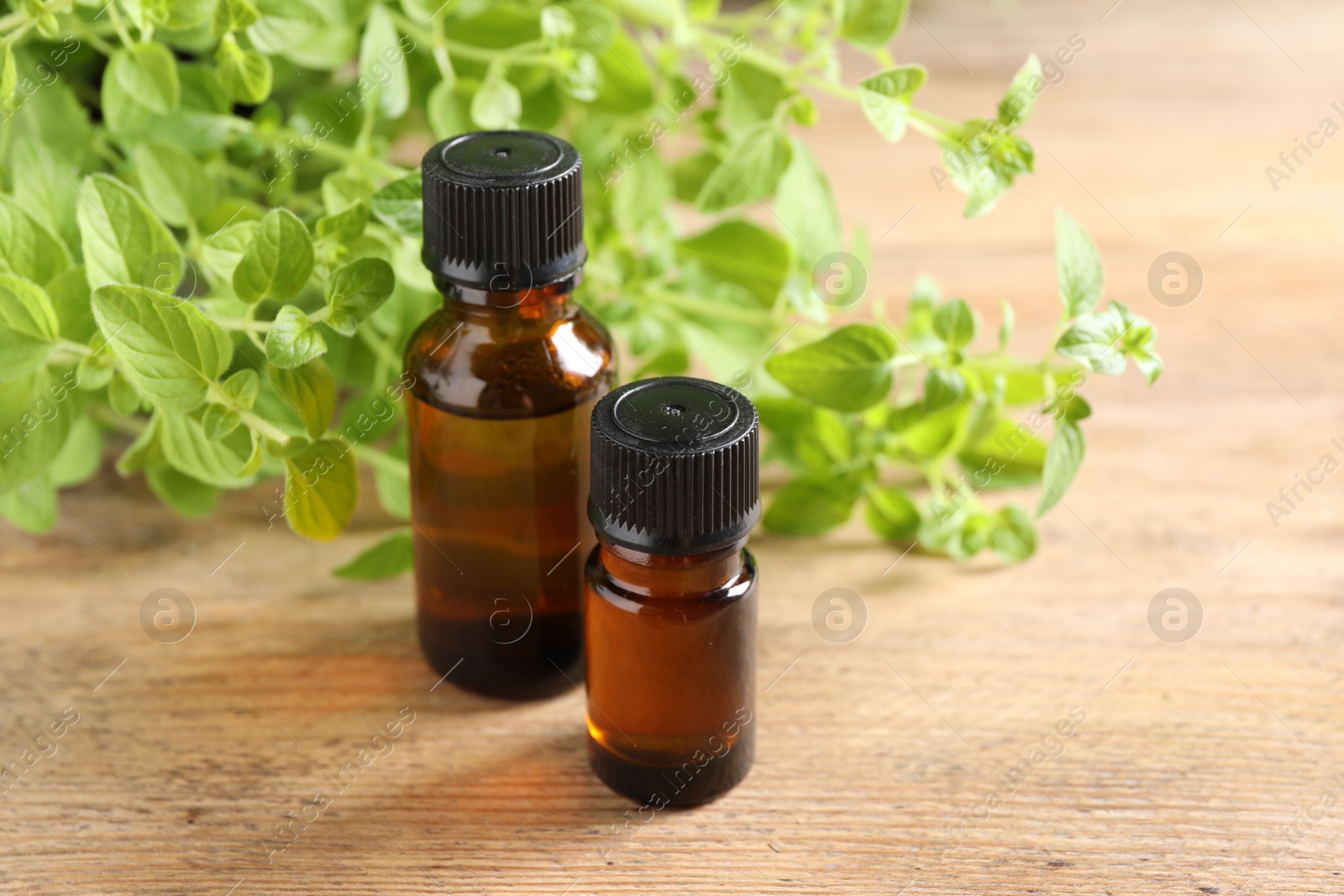 Photo of Essential oil in bottles and oregano twigs on wooden table, closeup