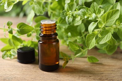 Photo of Essential oil in bottle and oregano twigs on wooden table, closeup