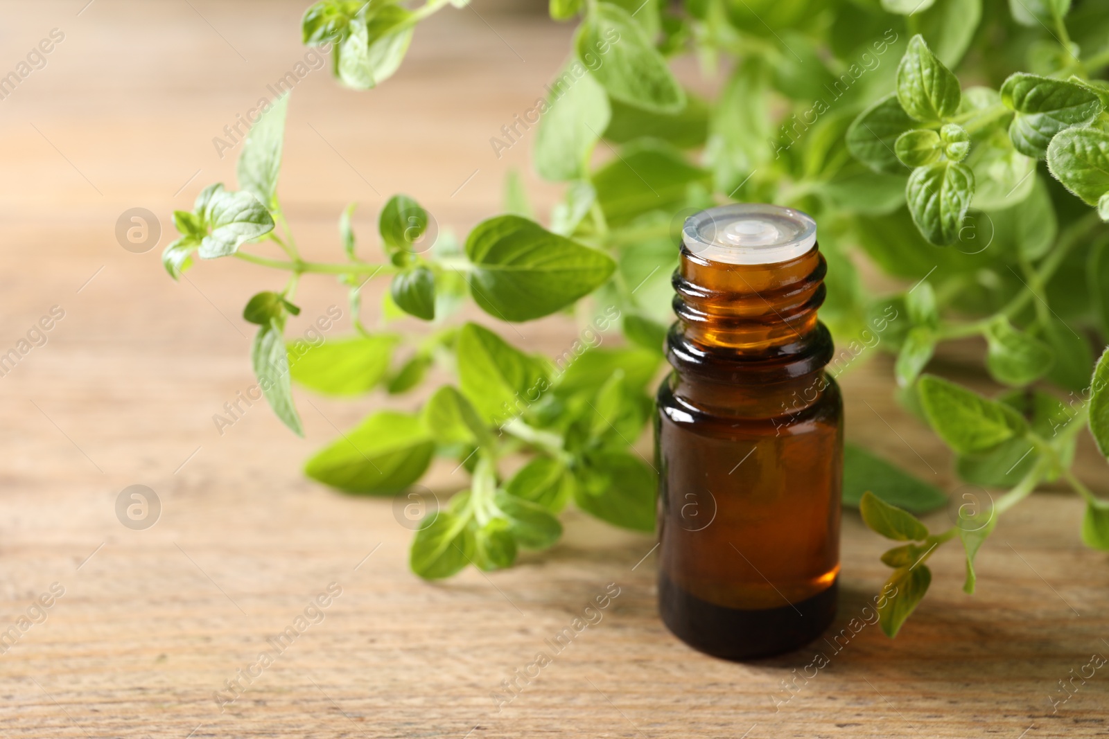 Photo of Essential oil in bottle and oregano twigs on wooden table, closeup