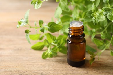 Photo of Essential oil in bottle and oregano twigs on wooden table, closeup