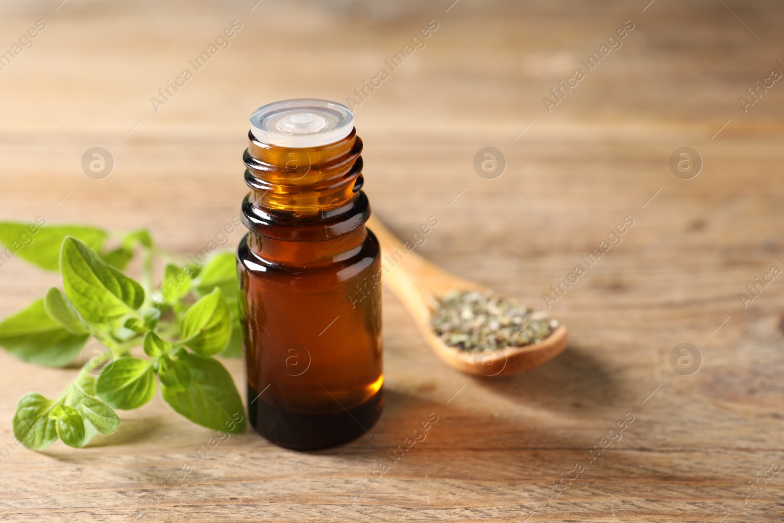 Photo of Essential oil in bottle, spoon with dry herb and oregano twigs on wooden table, closeup. Space for text