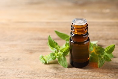 Essential oil in bottle and oregano twigs on wooden table, closeup. Space for text