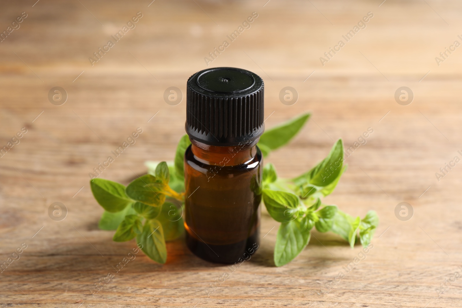 Photo of Essential oil in bottle and oregano twigs on wooden table, closeup