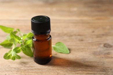 Photo of Essential oil in bottle and oregano twigs on wooden table, closeup. Space for text