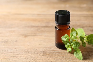 Photo of Essential oil in bottle and oregano twigs on wooden table, closeup. Space for text