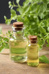 Essential oil in bottles and oregano twigs on wooden table, closeup