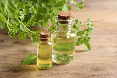 Essential oil in bottles and oregano twigs on wooden table, closeup