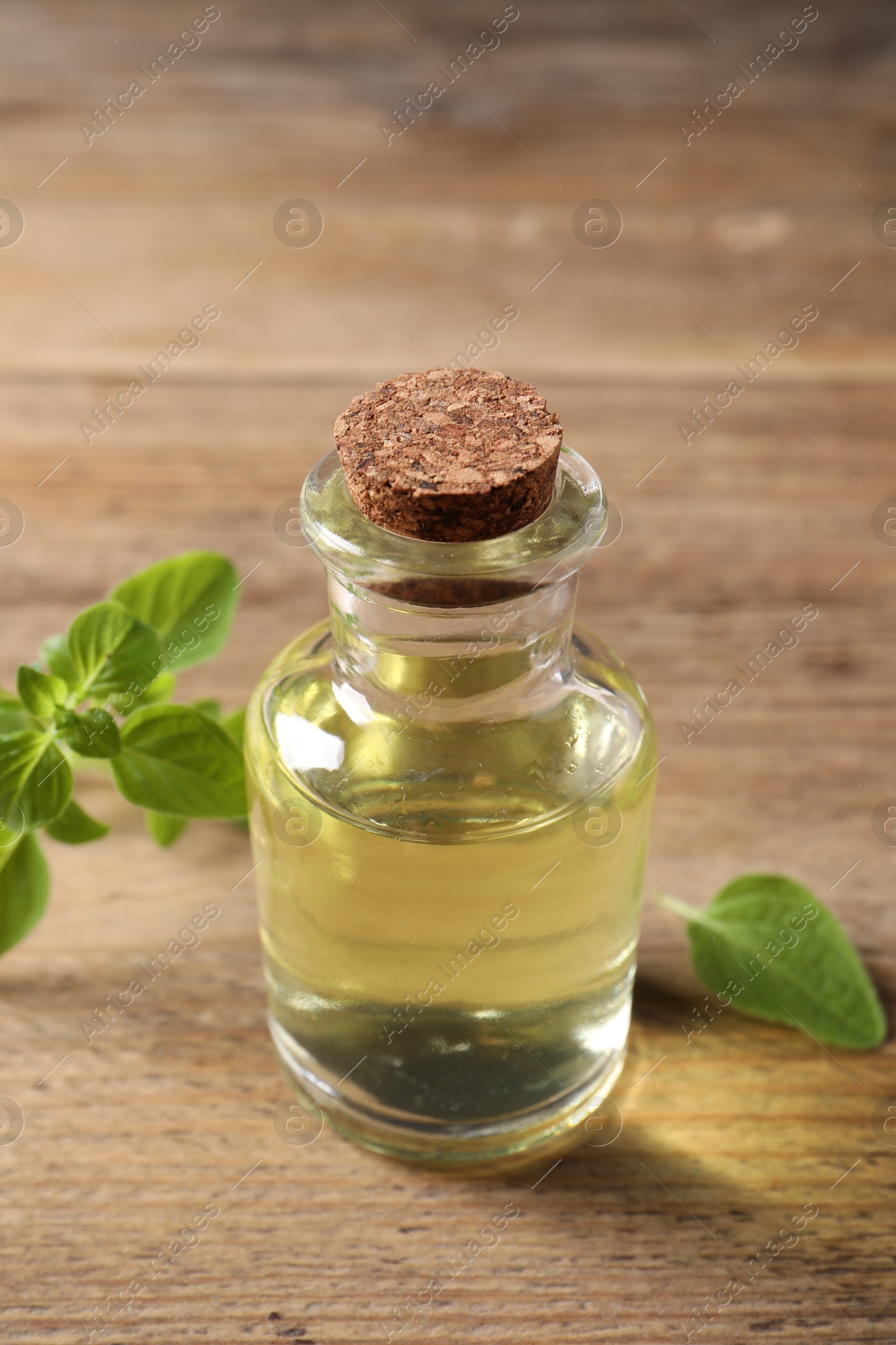 Photo of Essential oil in bottle and oregano leaves on wooden table, closeup