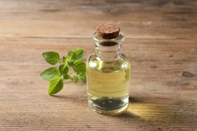 Photo of Essential oil in bottle and oregano twig on wooden table, closeup