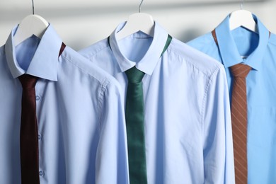 Photo of Hangers with shirts and neckties on light background, closeup