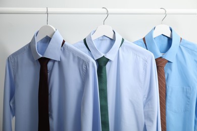 Photo of Hangers with shirts and neckties on light background