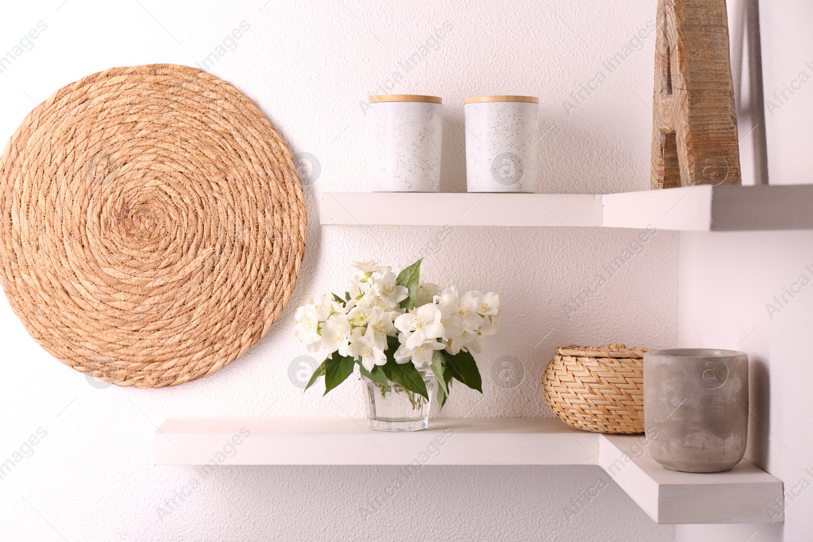 Photo of Beautiful jasmine flowers in vase and decor on shelves indoors