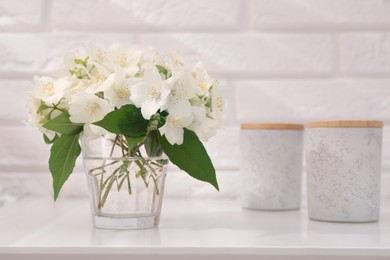 Photo of Beautiful jasmine flowers in vase and containers on white table