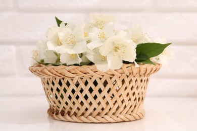 Photo of Beautiful jasmine flowers in wicker basket on white table