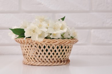 Photo of Beautiful jasmine flowers in wicker basket on white table. Space for text