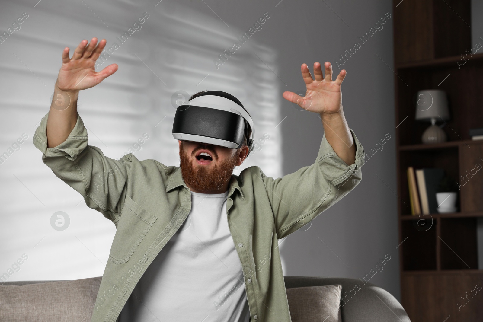 Photo of Emotional man using virtual reality headset on sofa at home