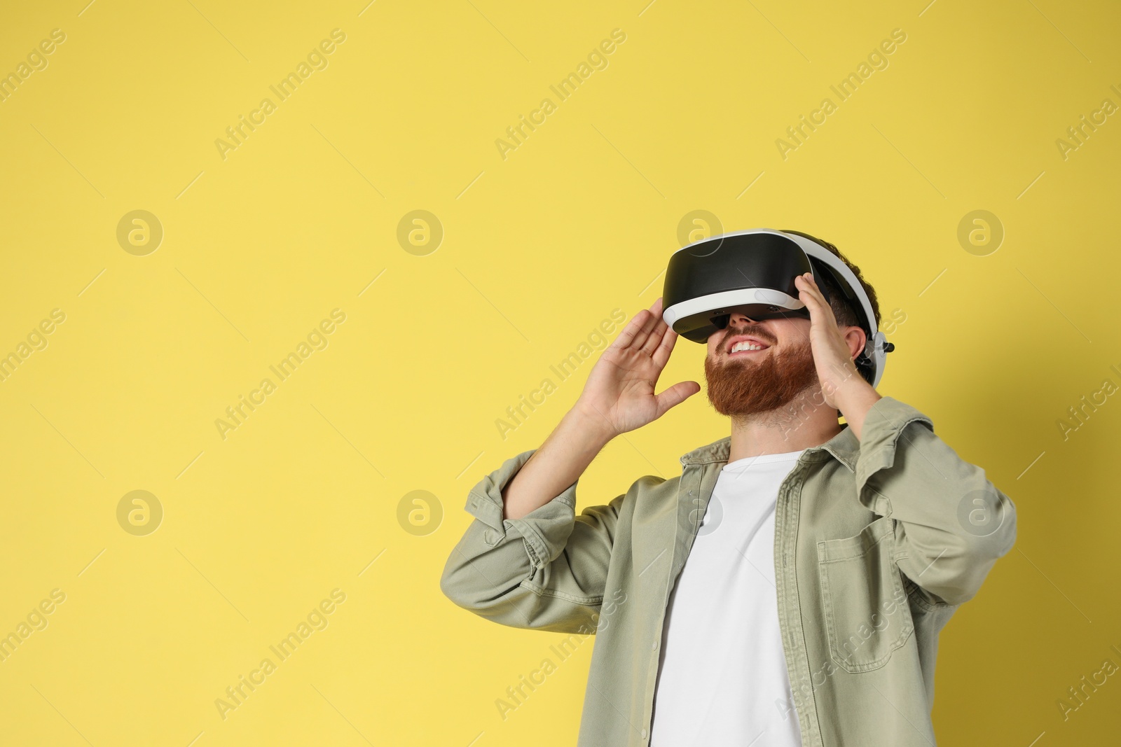 Photo of Happy man using virtual reality headset on pale yellow background. Space for text