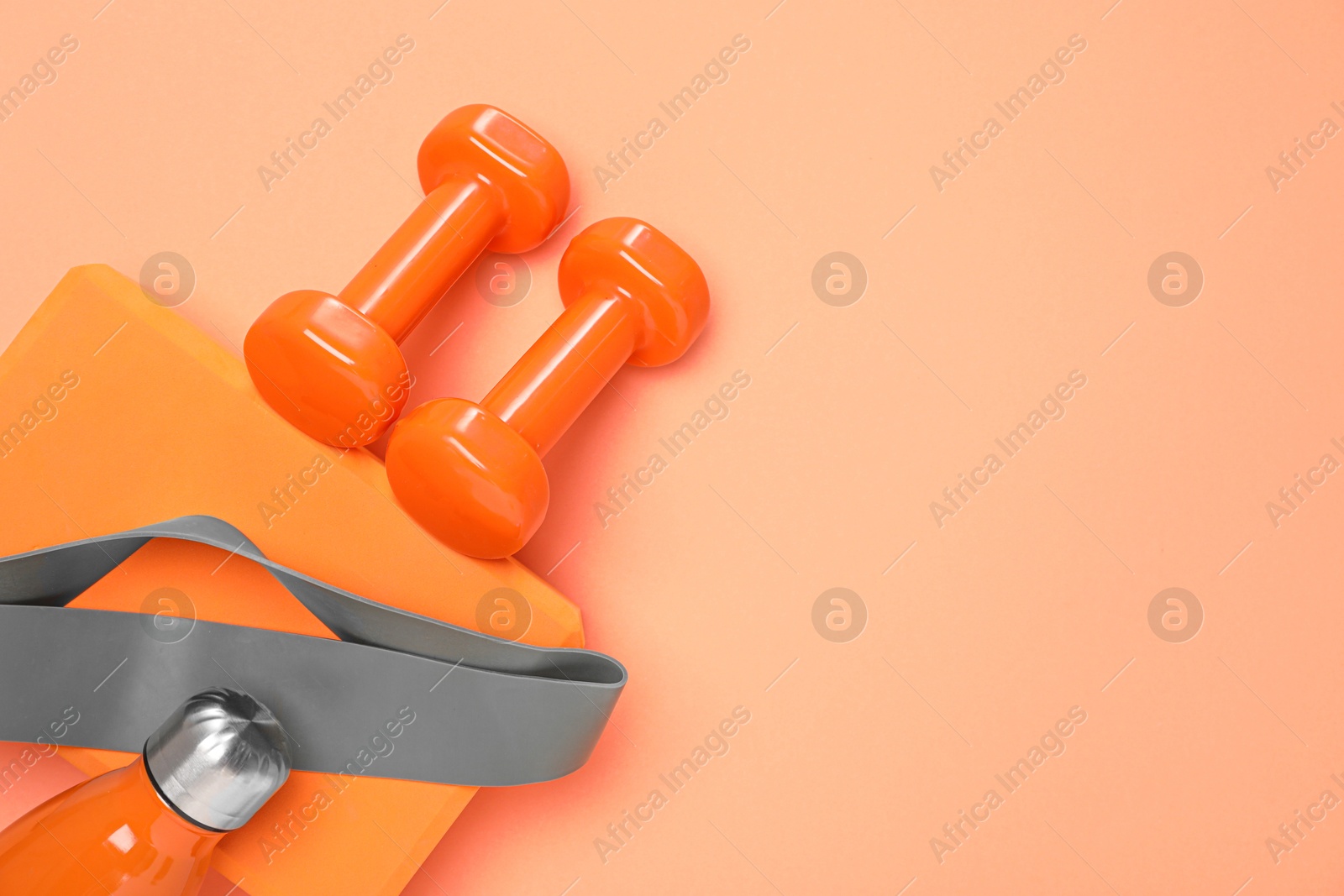 Photo of Dumbbells, thermo bottle, fitness elastic band and yoga block on coral background, flat lay. Space for text