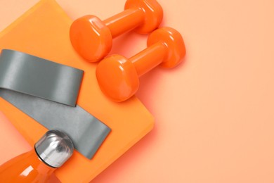 Photo of Dumbbells, thermo bottle, fitness elastic band and yoga block on coral background, flat lay. Space for text