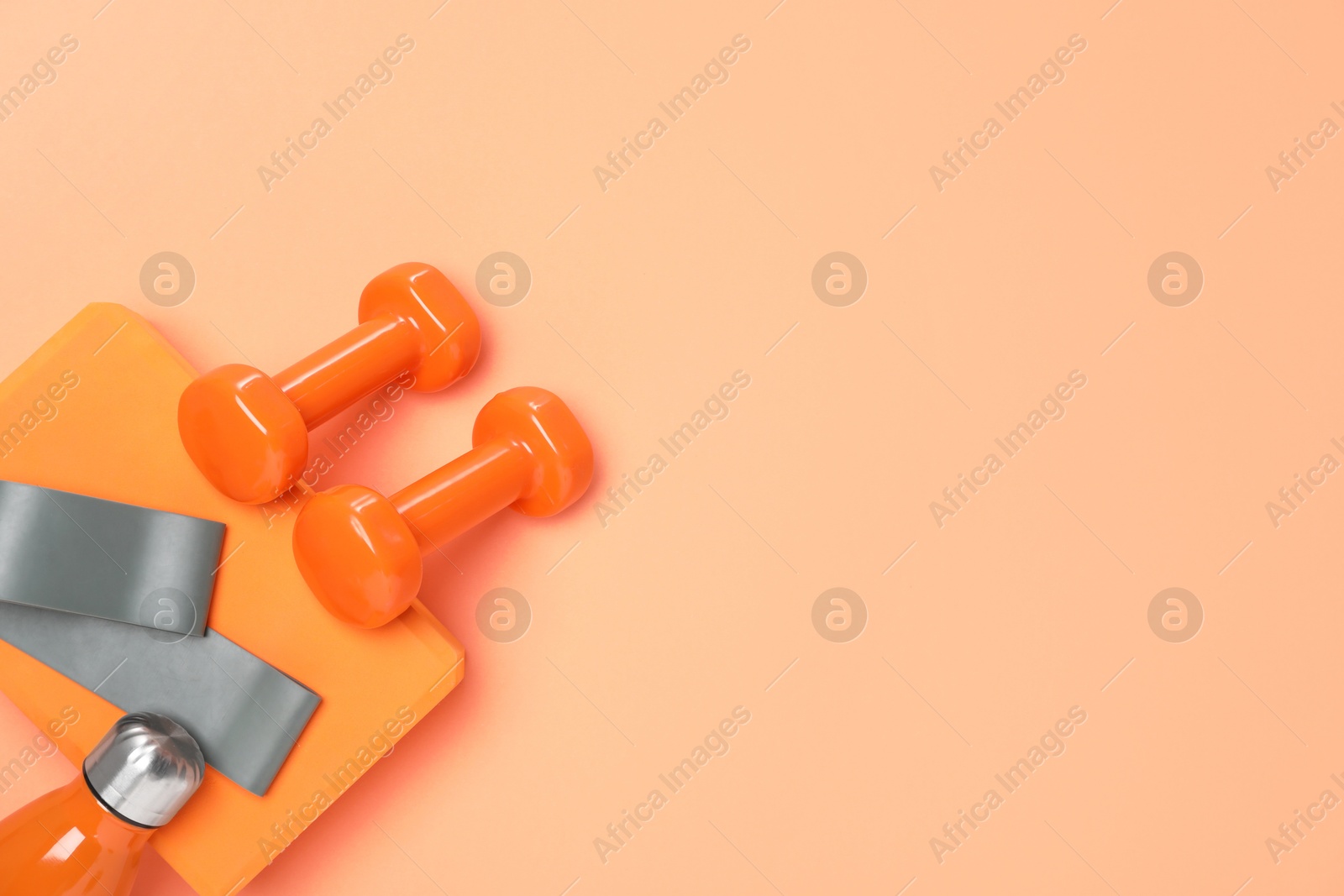 Photo of Dumbbells, thermo bottle, fitness elastic band and yoga block on coral background, flat lay. Space for text