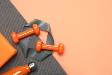 Photo of Dumbbells, thermo bottle, fitness elastic band, yoga block and mat on coral background, flat lay. Space for text