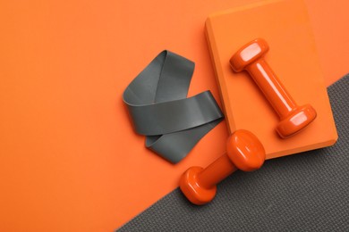 Photo of Dumbbells, yoga block, mat and fitness elastic band on orange background, flat lay. Space for text