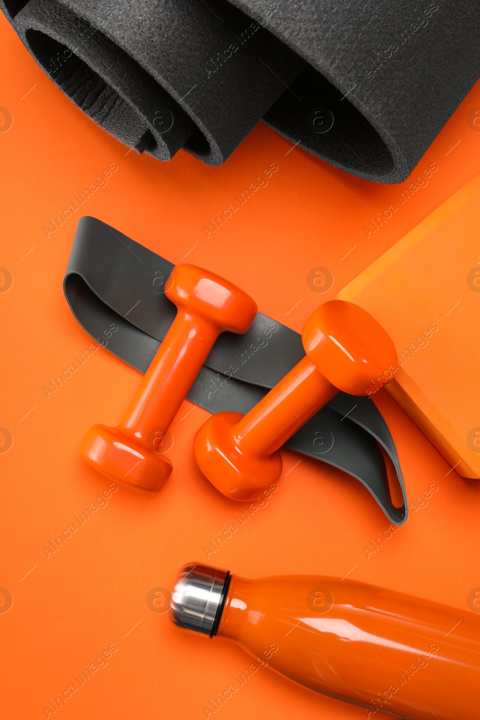 Photo of Dumbbells, yoga block, mat, thermo bottle and fitness elastic band on orange background, flat lay