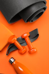 Photo of Dumbbells, yoga block, mat, thermo bottle and fitness elastic band on orange background, flat lay