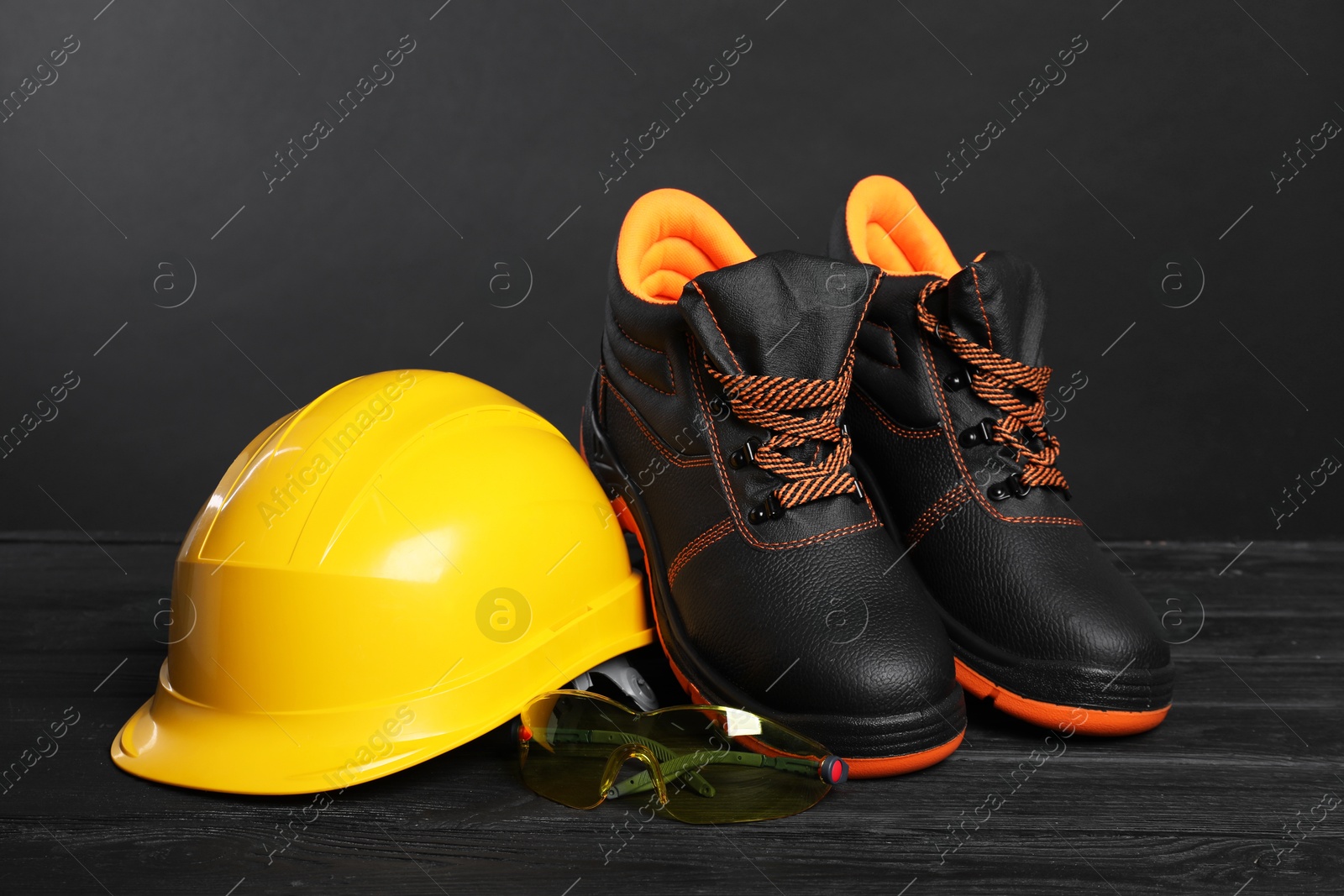 Photo of Pair of working boots, hard hat and goggles on black wooden surface