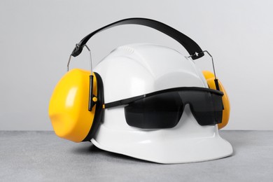 Photo of Hard hat with earmuffs and goggles on gray surface against light background