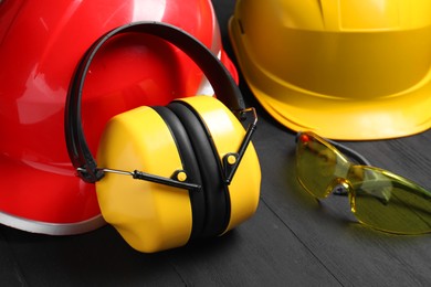 Photo of Hard hats, earmuffs and goggles on black wooden background, closeup