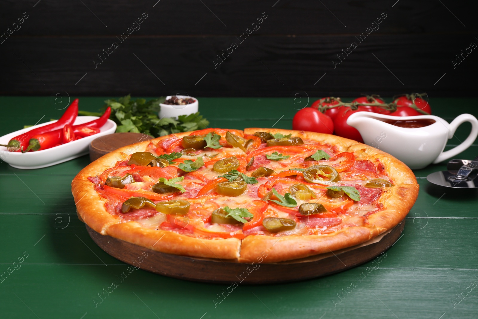 Photo of Delicious pizza Diablo, ingredients and cutter on green wooden table