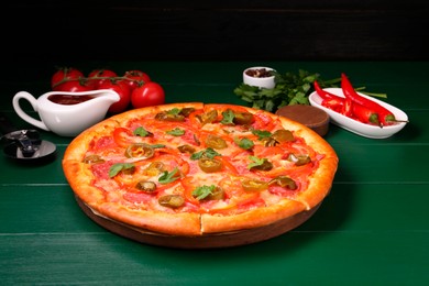 Photo of Delicious pizza Diablo, ingredients and cutter on green wooden table