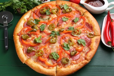 Photo of Delicious pizza Diablo, ingredients and cutter on green wooden table