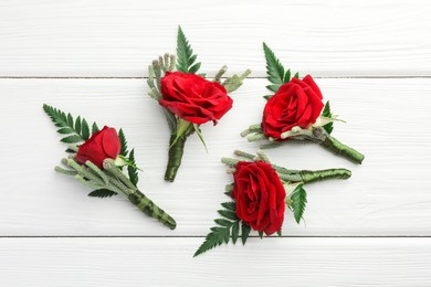 Photo of Many stylish red boutonnieres on white wooden table, flat lay