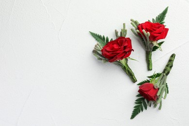 Photo of Many stylish red boutonnieres on white textured table, flat lay. Space for text