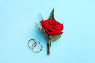 Photo of Small stylish boutonniere and rings on light blue background, top view