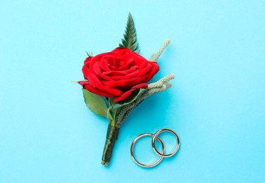 Photo of Small stylish boutonniere and rings on light blue background, top view