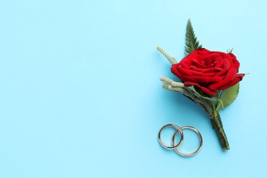 Photo of Small stylish boutonniere and rings on light blue background, top view. Space for text