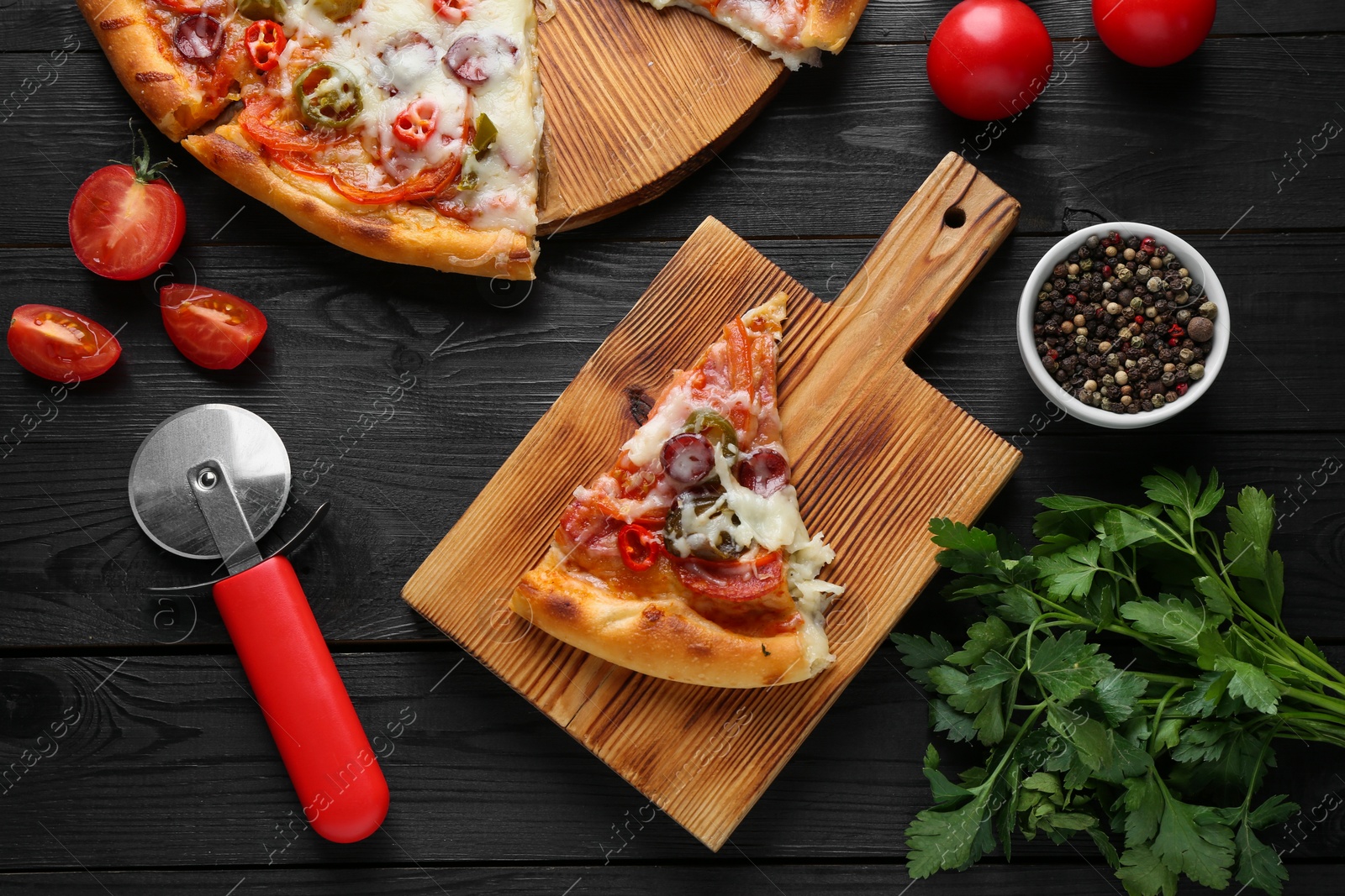 Photo of Delicious pizza Diablo, tomatoes, parsley, peppercorns and cutter on black wooden table, flat lay