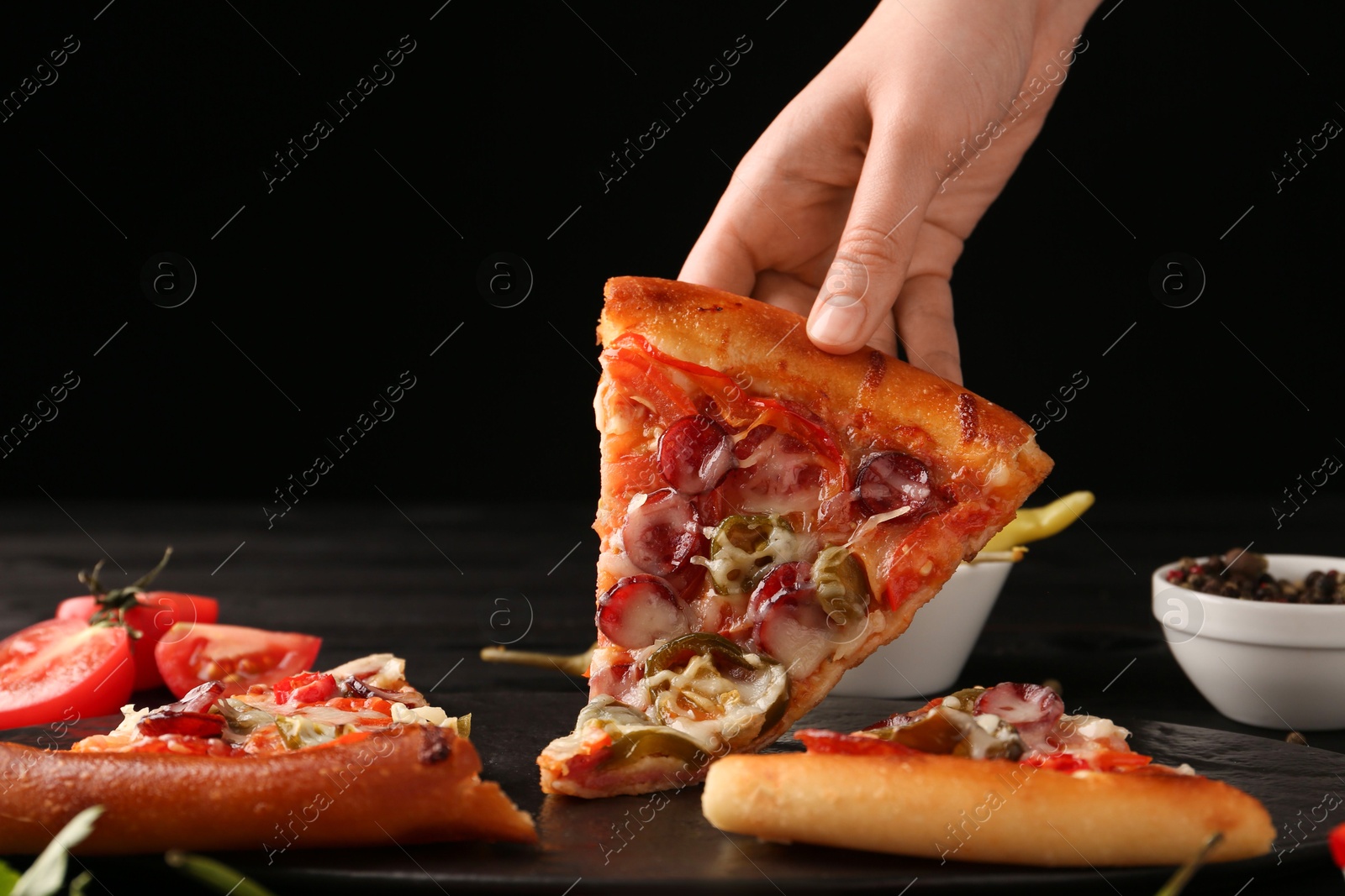 Photo of Woman taking piece of delicious pizza Diablo at table on black background, closeup