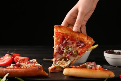 Photo of Woman taking piece of delicious pizza Diablo at table on black background, closeup