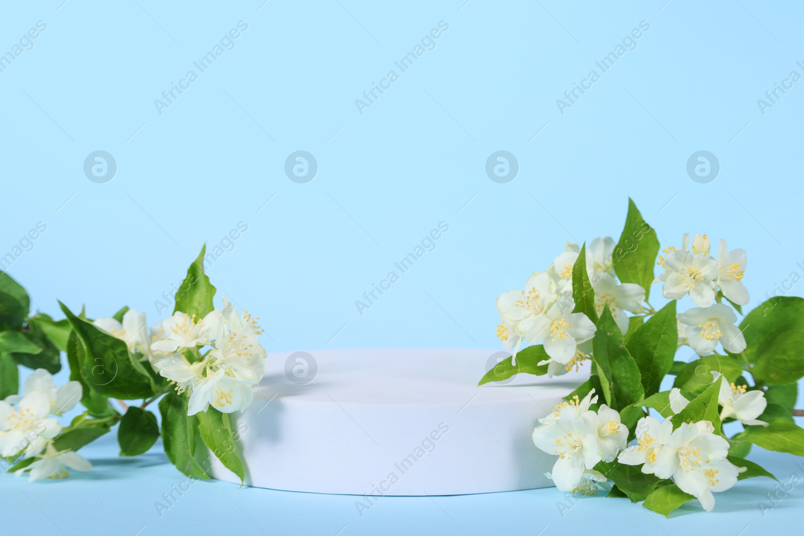 Photo of Presentation of product. White podium and beautiful jasmine flowers on light blue background, space for text