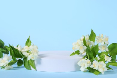 Photo of Presentation of product. White podium and beautiful jasmine flowers on light blue background, space for text