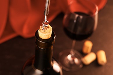 Photo of Wine bottle with corkscrew, glass and corks on table, closeup